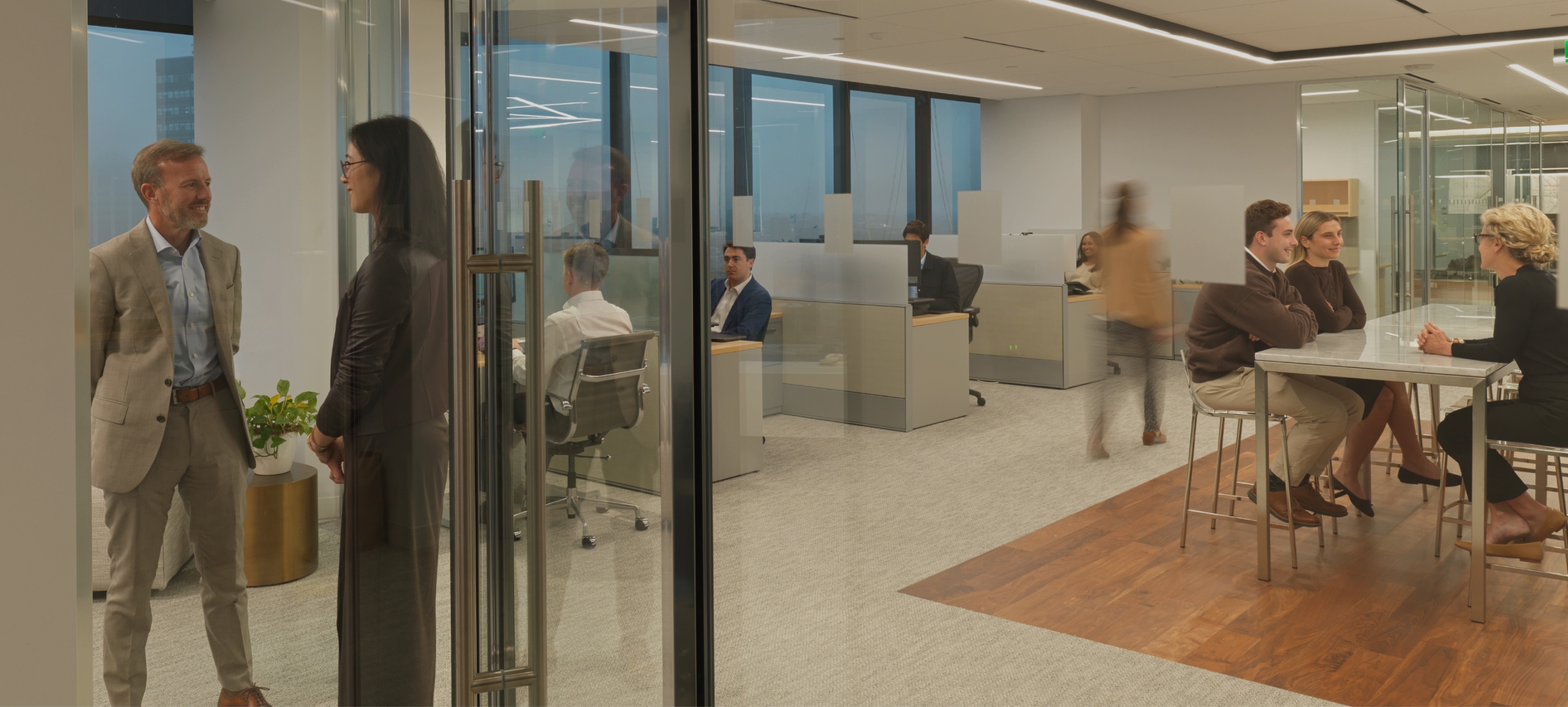 Professionals talking in a modern open-plan office, with coworkers meeting at a high table in the break area.
