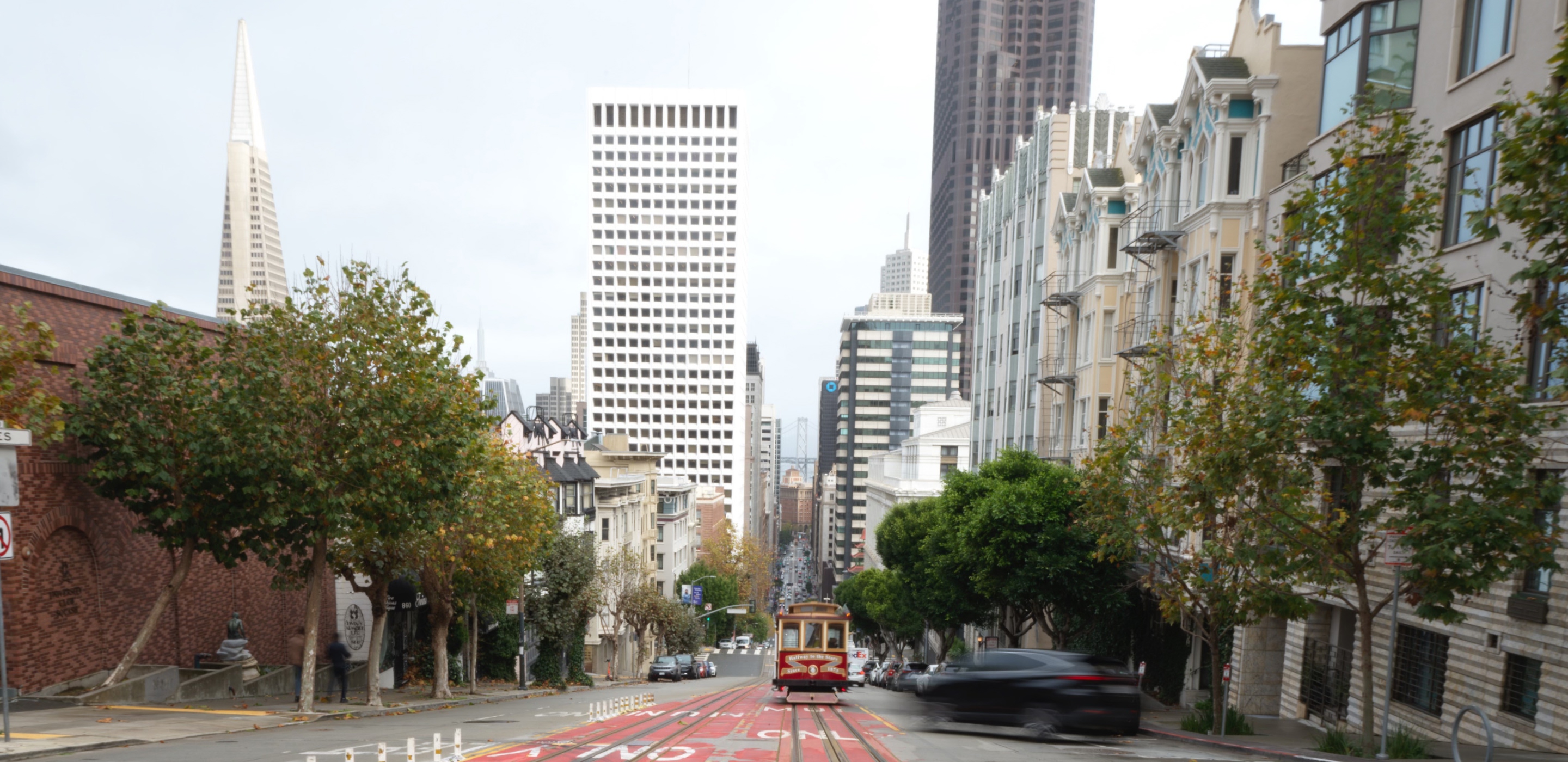San Francisco cable car on a steep downtown street with the city skyline in the background.