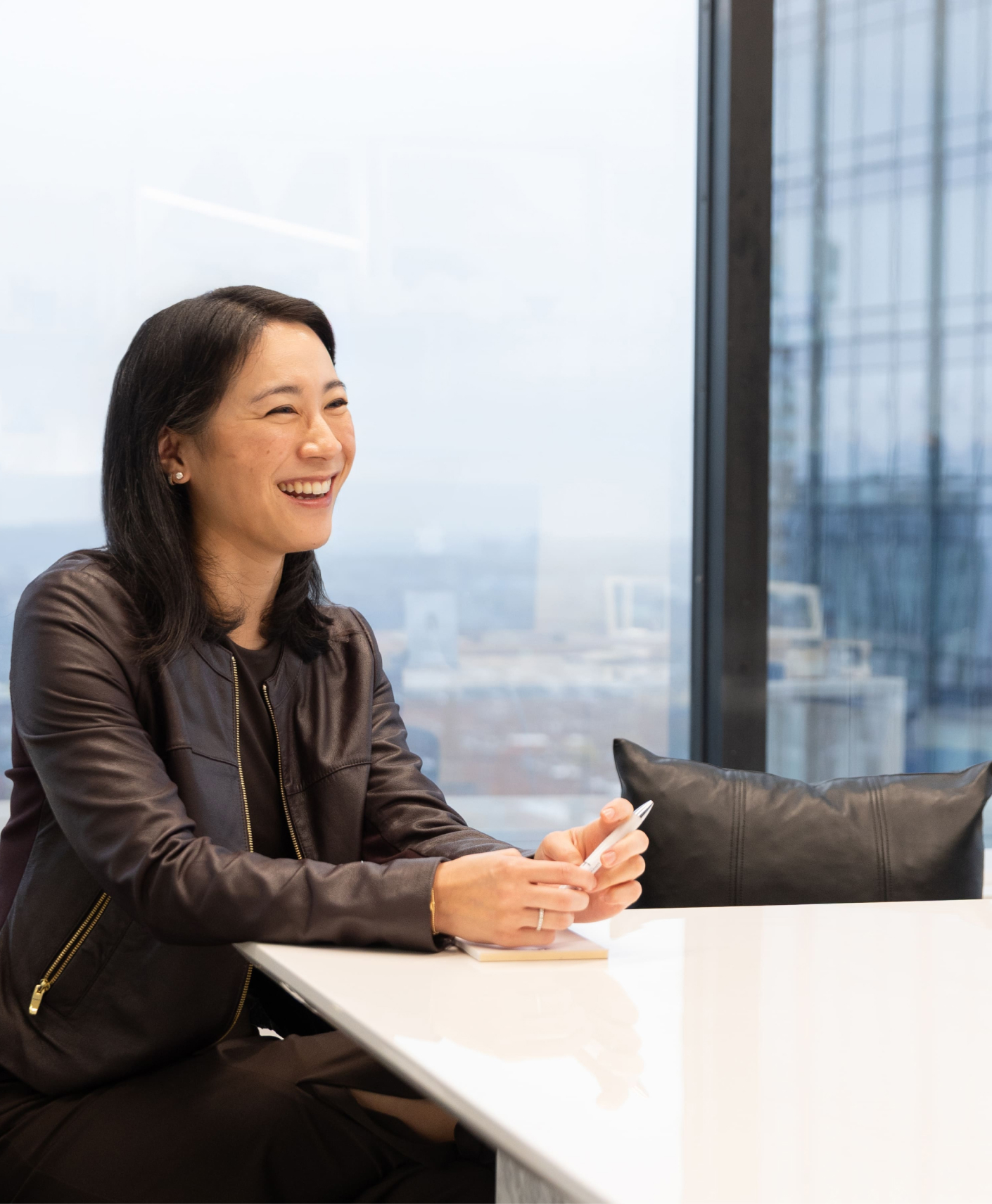 Smiling colleague holding a pen while seated at a conference table in a bright office.