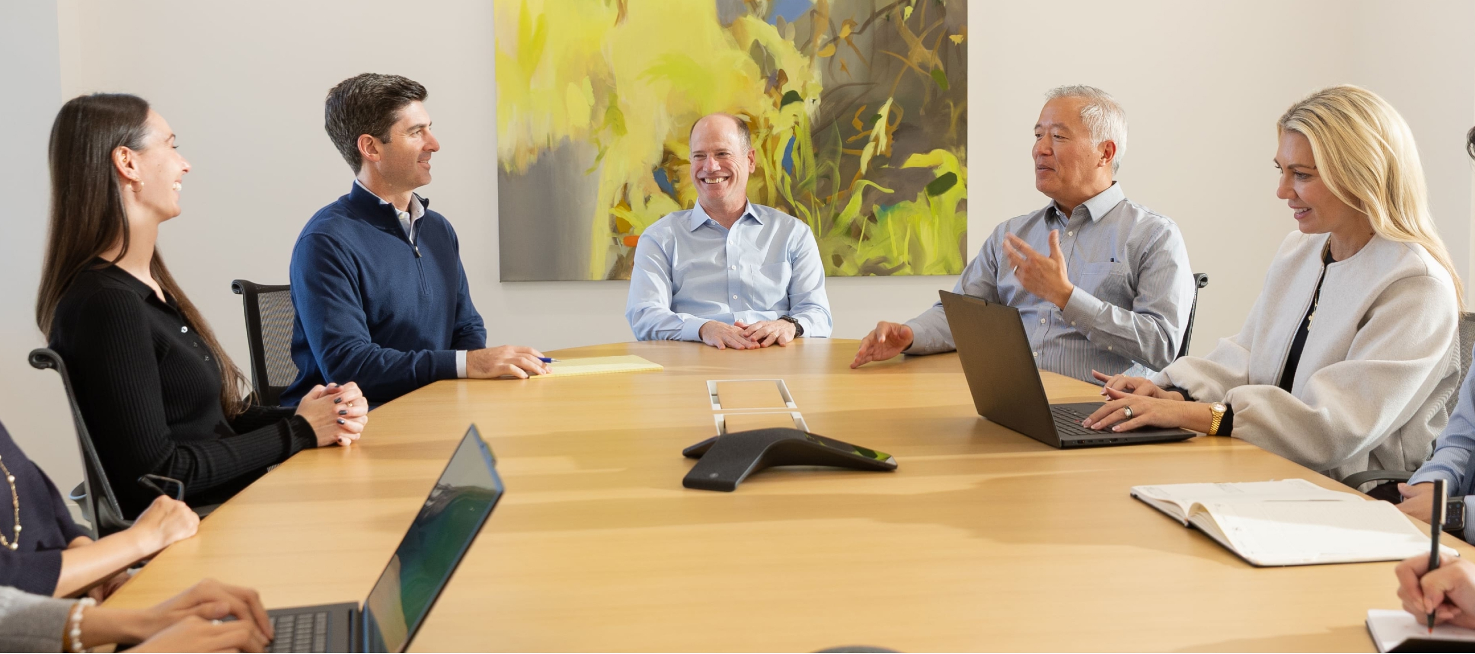 Team meeting around a conference table with laptops and notes in a modern office.