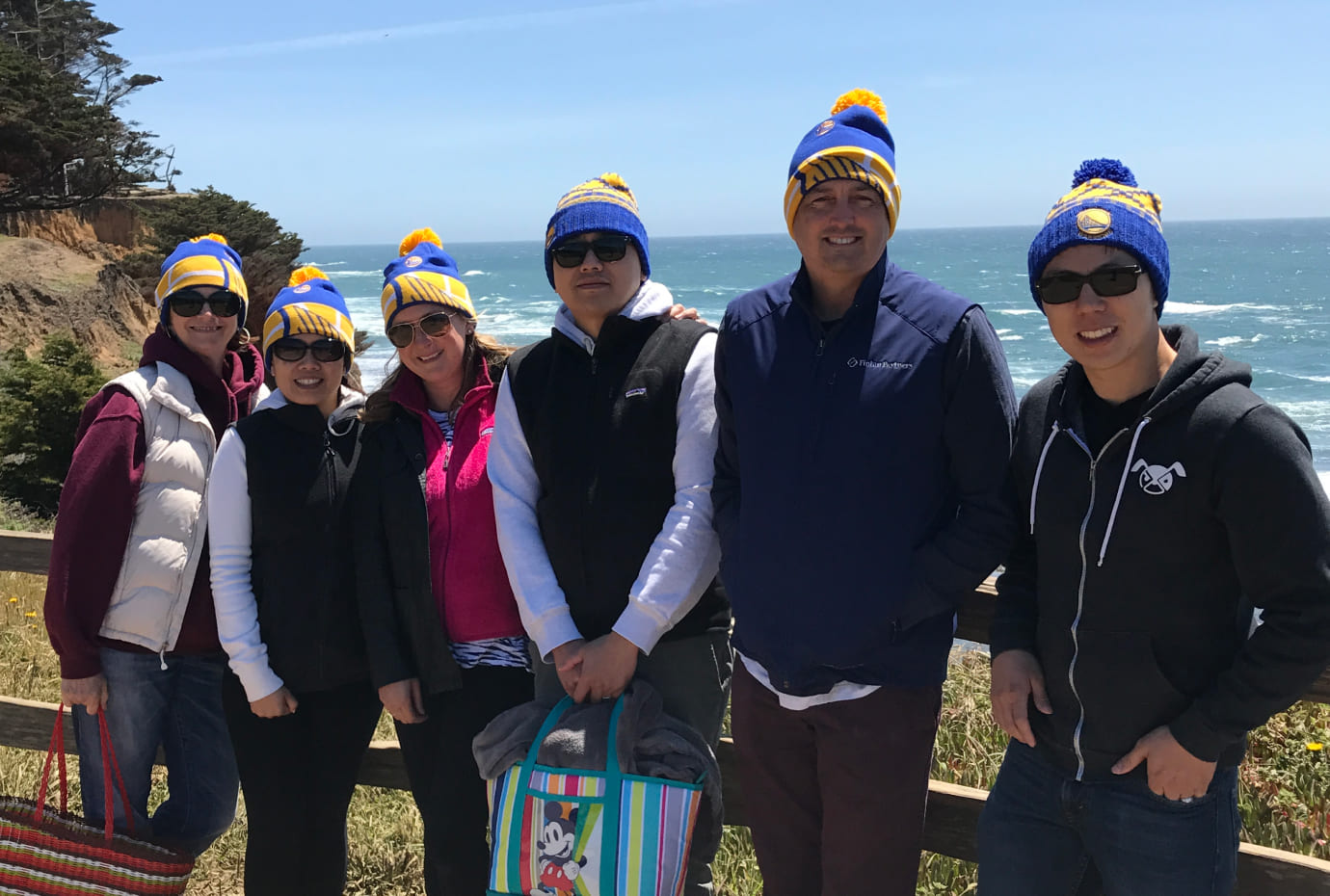 Group photo of colleagues wearing matching beanies on a coastal overlook with the ocean in the background.