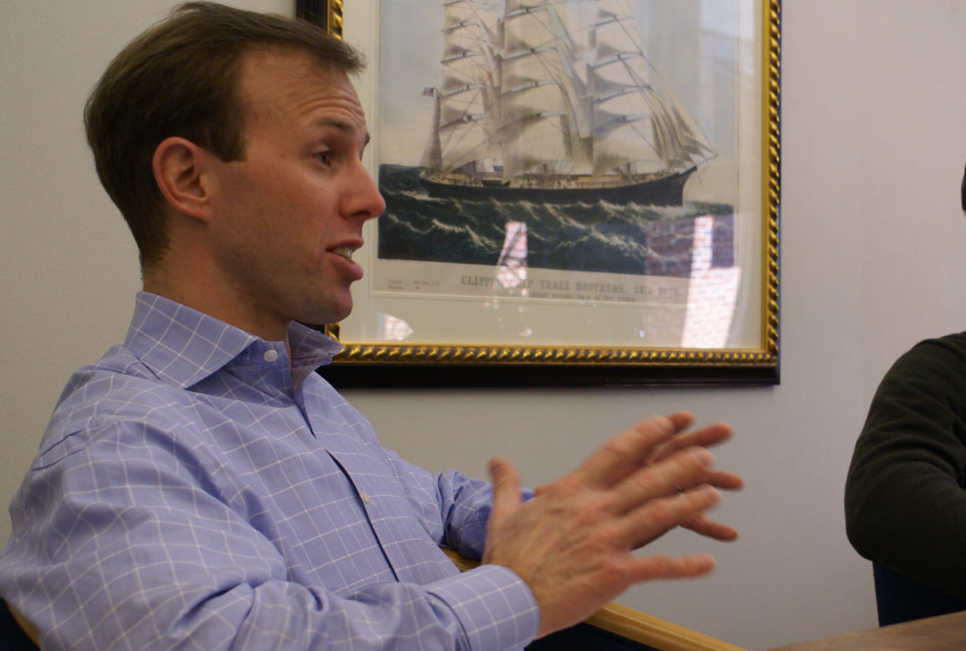 Colleague speaking and gesturing during a meeting, with framed artwork on the wall behind him.