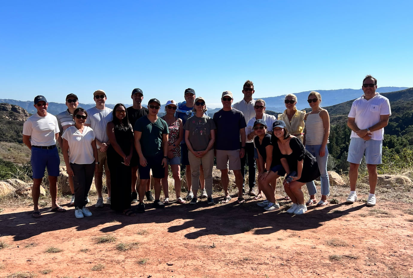 Group photo of colleagues on a scenic outdoor hike with hills and blue sky in the background.