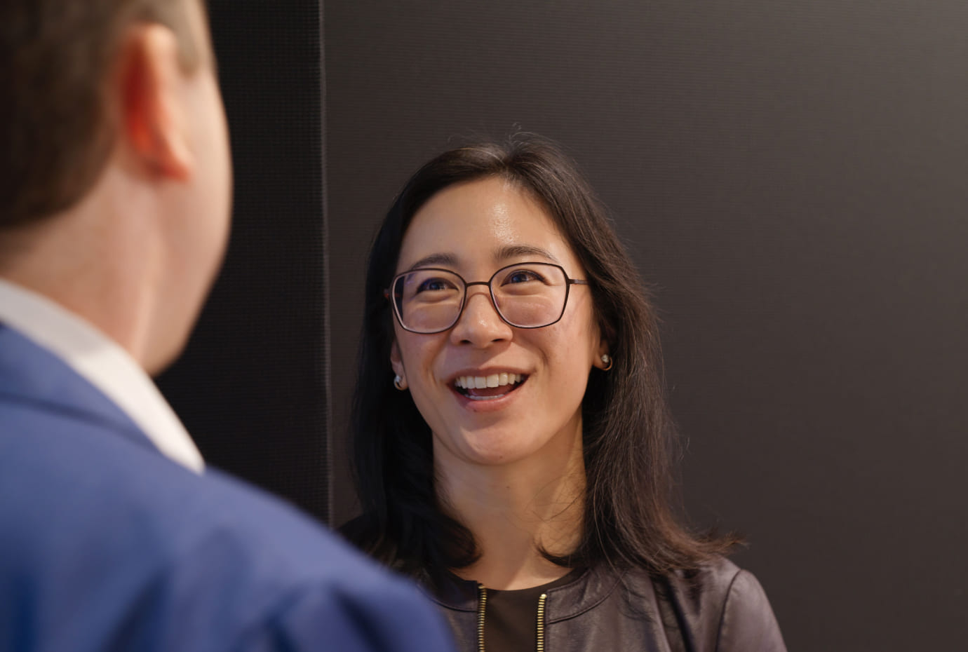Colleagues chat in the office as one person smiles during conversation.