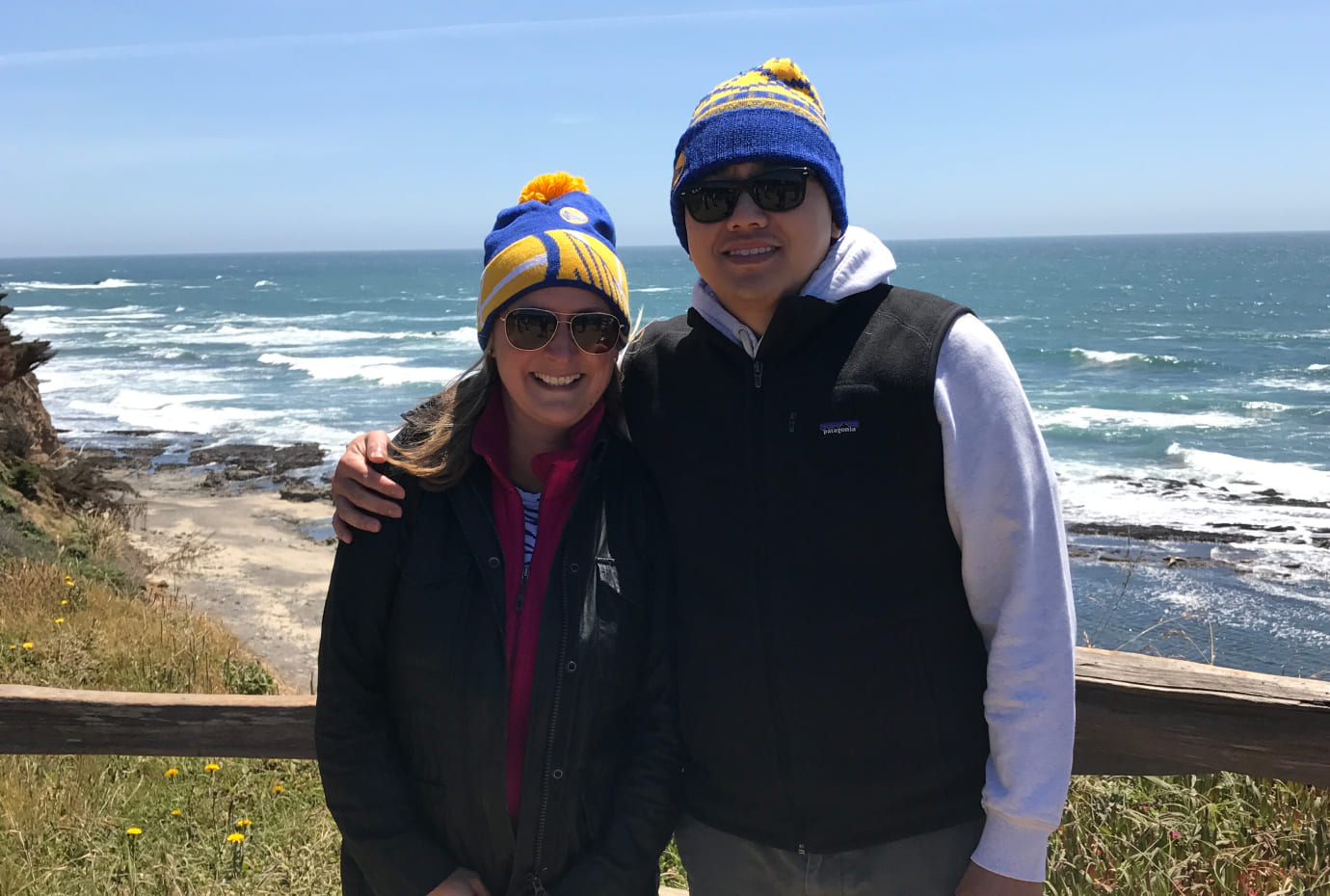 Two Fisher Lynch team members wearing matching knit hats pose by the ocean during a coastal outing.